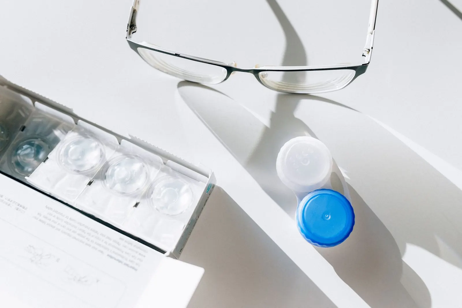 Eyeglasses next to a contact lens case and daily lens blisters